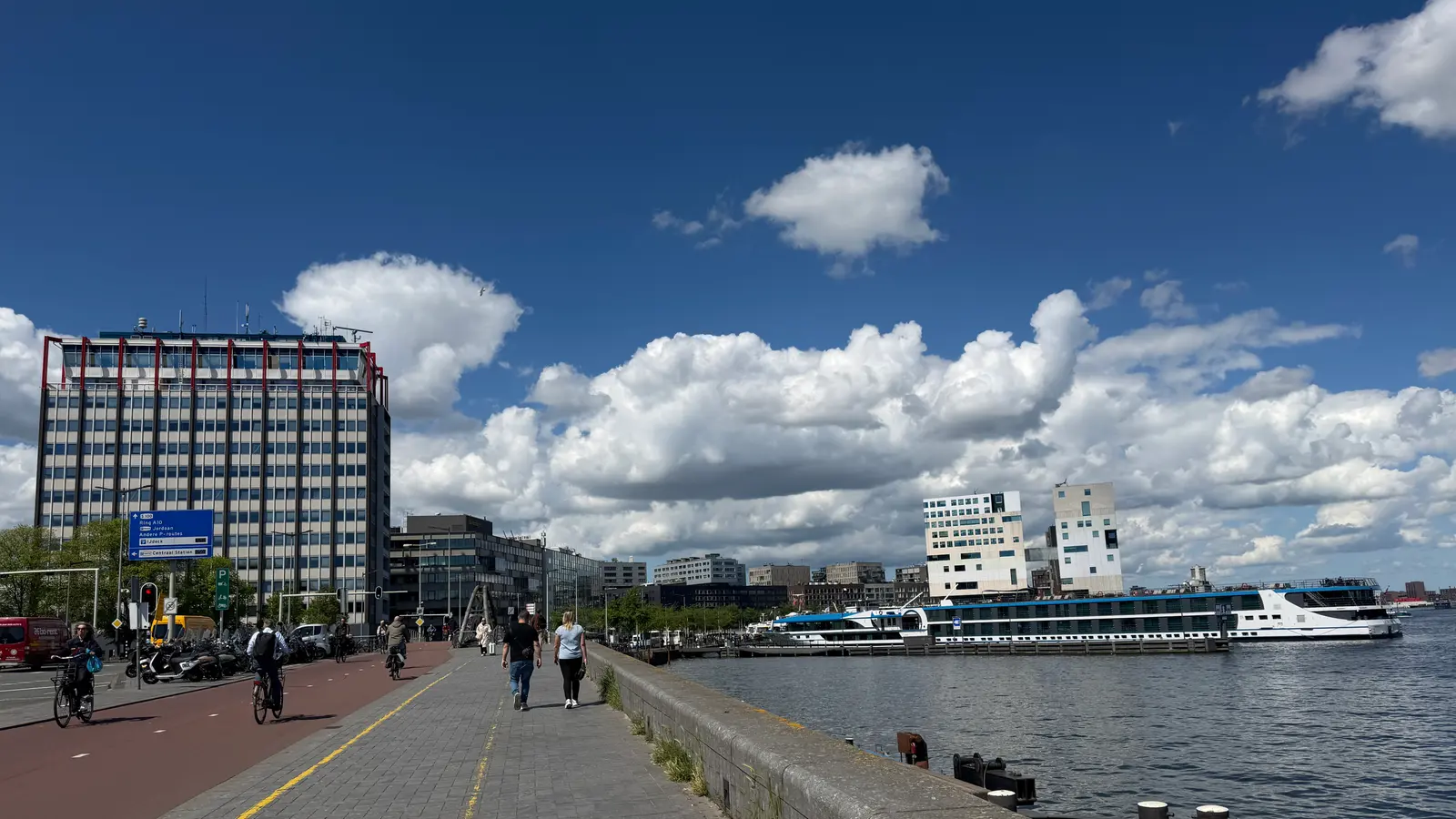 The Havengebouw harbour building on the IJ waterfront in Amsterdam, with vessels moored along the quay.