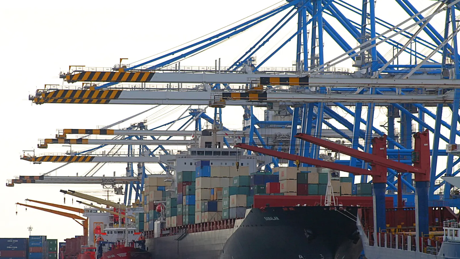 Gantry cranes working a container ship at a Mediterranean terminal, with stacked containers on deck.