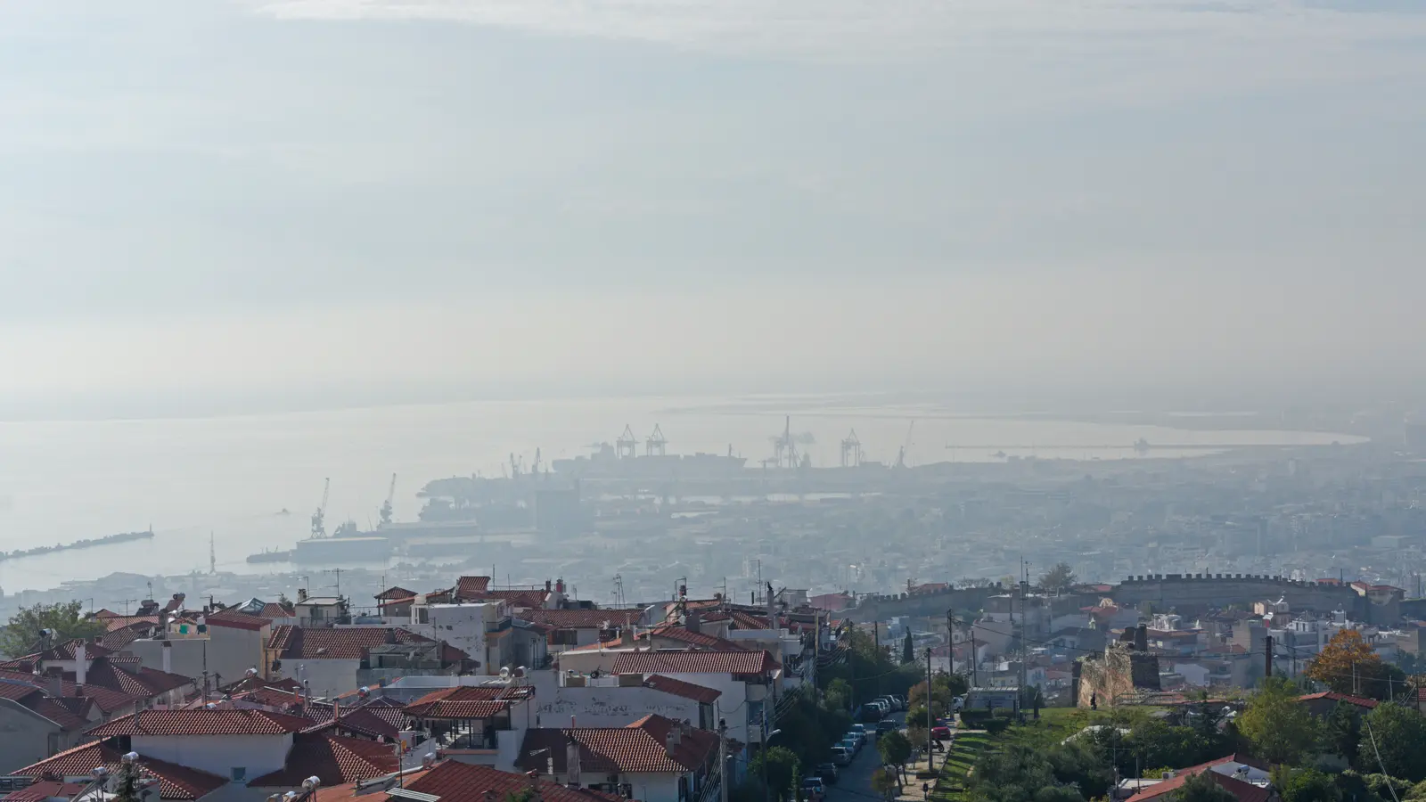 The port of Thessaloniki seen from the hills above the city, with quays and cranes along the waterfront.